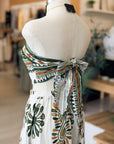 Mannequin wearing a white dress with green and orange floral patterns in a blurred indoor setting.