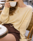 Woman in a yellow sweater holding a cup of coffee outdoors.