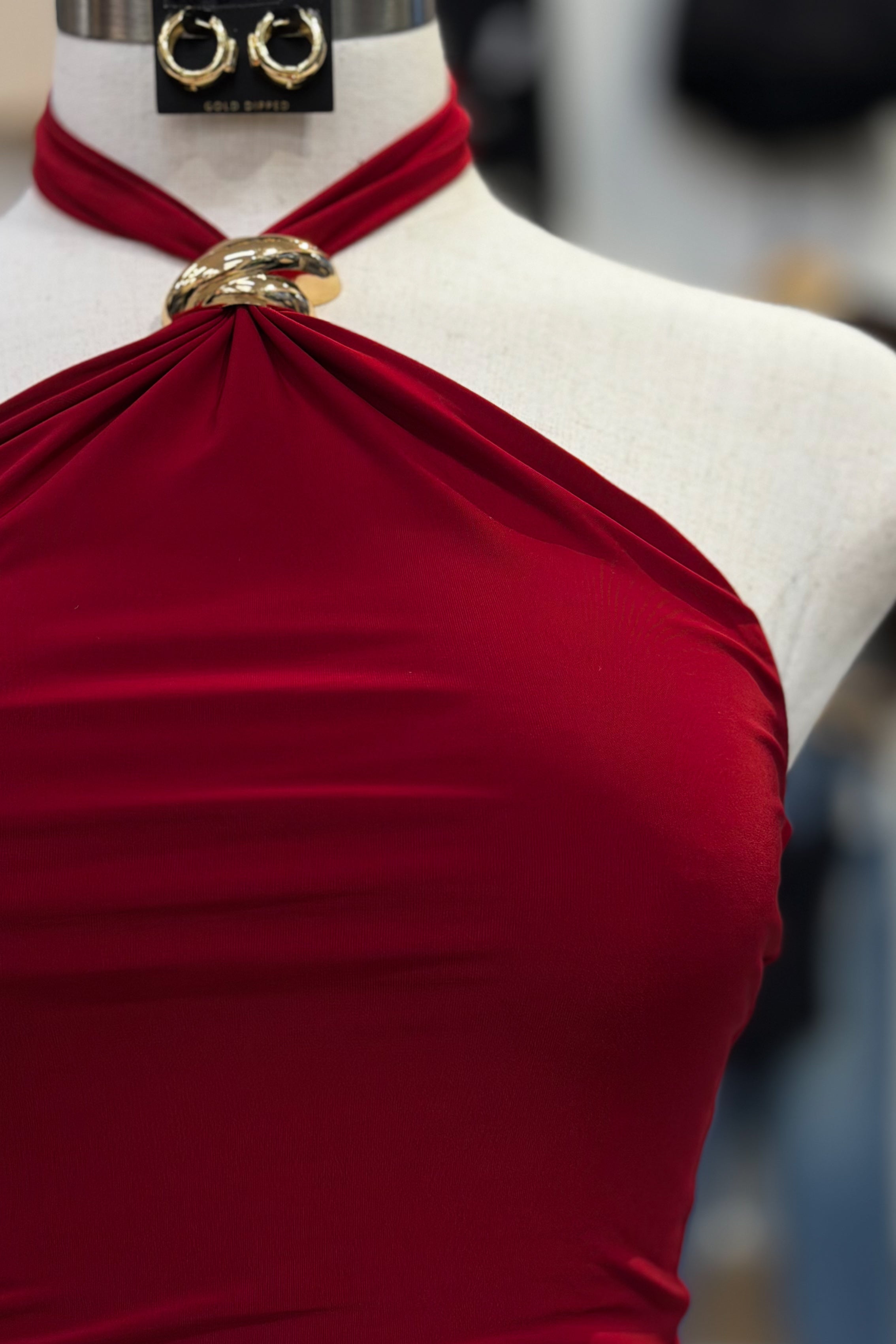 Red halter top on a mannequin with gold jewelry, against a blurred background.