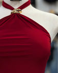 Red halter top on a mannequin with gold jewelry, against a blurred background.