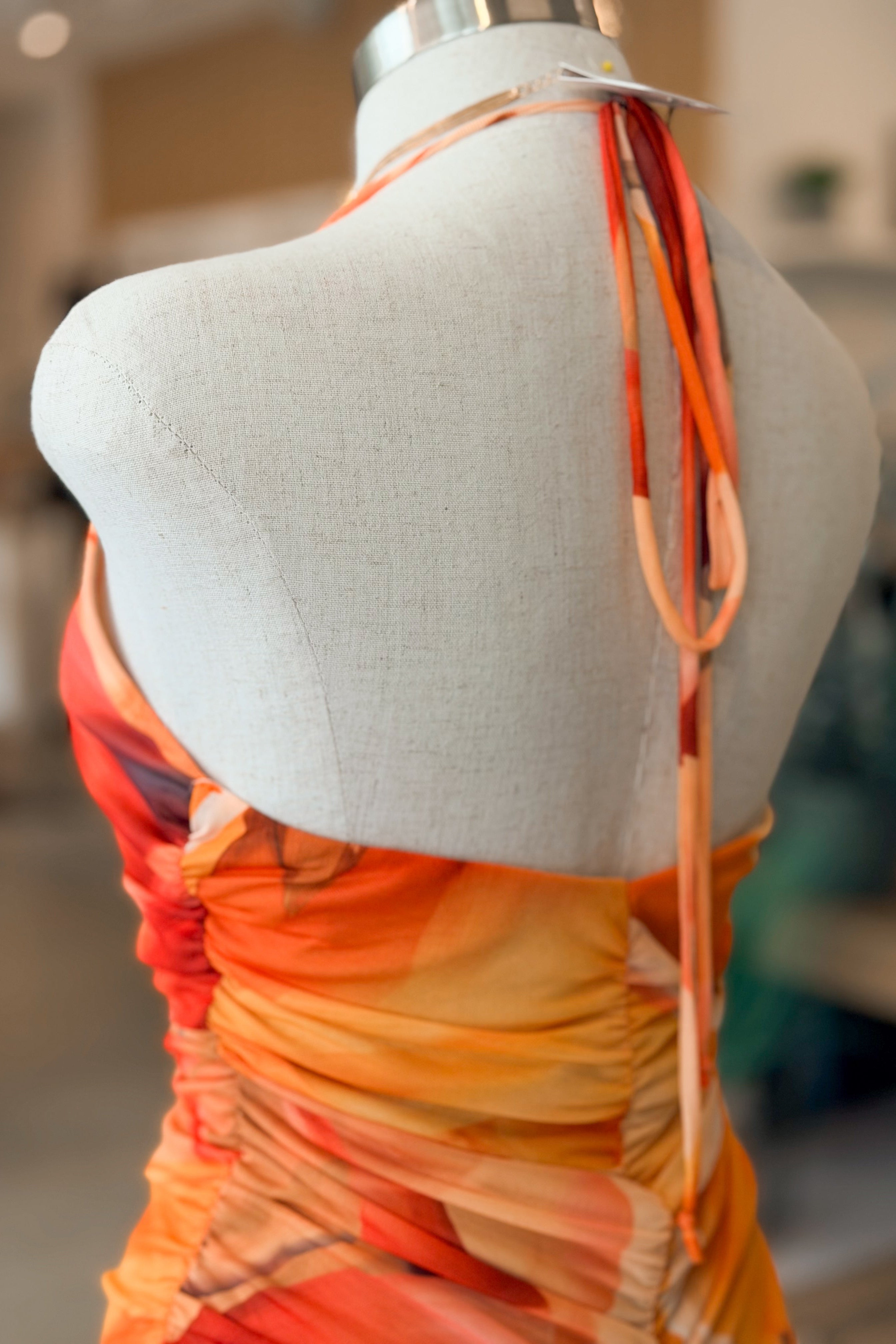 Mannequin wearing a colorful dress with orange and yellow gradient on a blurred indoor background